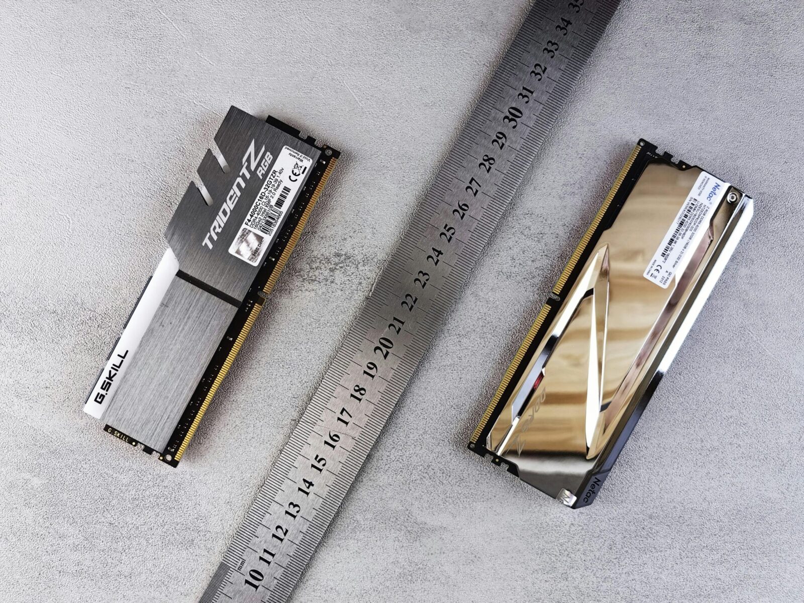 Close-up of computer memory modules and metal ruler placed on a textured gray surface.